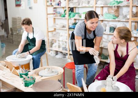 Töpferin unterrichtet junge Lehrlinge in der Werkstatt, wie man Töpferei auf Töpferrad macht Stockfoto