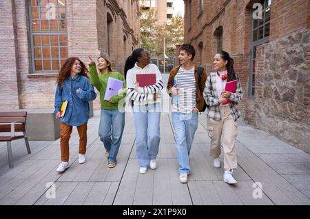 Glückliche Studenten schlendern mit Arbeitsbüchern über den Universitätscampus und trinken Kaffee. Stockfoto