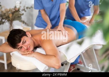 Entspannter Mann, der eine Rückenmassage durch zwei Masseure erlebt hat Stockfoto