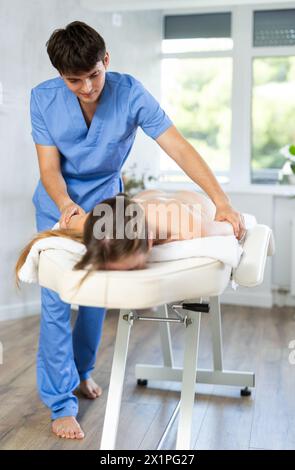 Professioneller junger Masseur mit Rückenmassage für Patientin Stockfoto