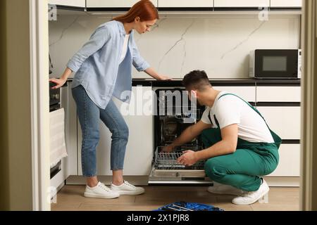 Frau, die sieht, wie ein Soldat ihren Geschirrspüler in der Küche repariert Stockfoto