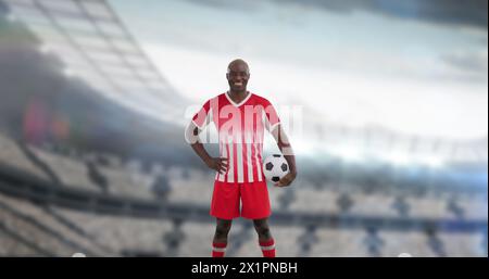 Mann in rot-weißer Fußballuniform, der Ball hält, auf einem Feld steht Stockfoto