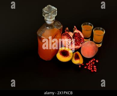 Hausgemachter Obstlikör in einer Flasche und zwei Gläsern auf schwarzem Hintergrund, neben Stücken eines Reifen Pfirsichs und einer gebrochenen Granatapfelfrucht. Nahaufnahme. Stockfoto