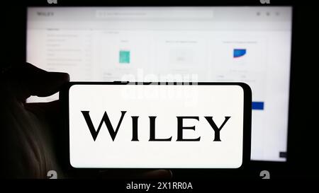 Person, die ein Mobiltelefon mit dem Logo des US-Verlags John Wiley and Sons Inc. Vor der Webseite des Unternehmens hält. Schwerpunkt auf dem Display des Telefons. Stockfoto