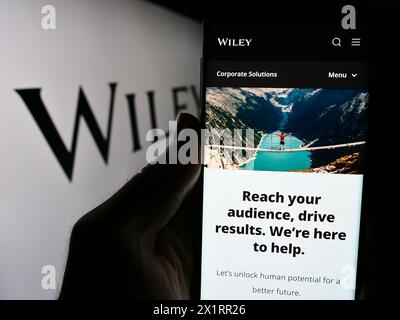 Person, die ein Mobiltelefon hält, mit Webseite des US-Verlags John Wiley and Sons Inc. Vor dem Logo. Konzentrieren Sie sich auf die Mitte des Telefondisplays. Stockfoto