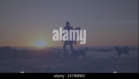 Kaukasischer Mann, der mit zwei Hunden am Strand läuft und Surfbrett hält Stockfoto