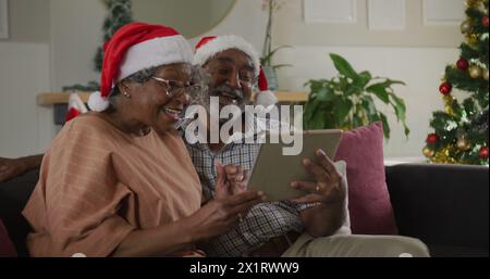 Ein hochrangiges birassisches Paar mit Weihnachtsmützen und Blick auf ein Tablet Stockfoto