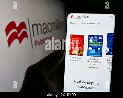 Person, die ein Handy hält, mit Webseite des britischen Verlags Macmillan Publishers vor dem Logo. Konzentrieren Sie sich auf die Mitte des Telefondisplays. Stockfoto