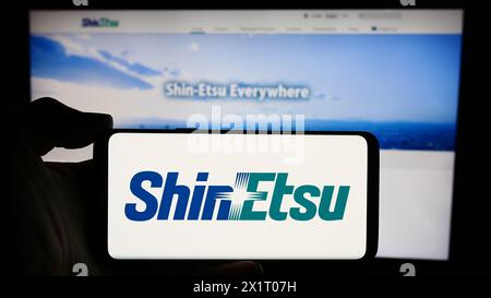 Person, die ein Mobiltelefon mit dem Logo des japanischen Chemieunternehmens Shin-Etsu Chemical Co. Ltd. Vor der Webseite hält. Schwerpunkt auf dem Display des Telefons. Stockfoto