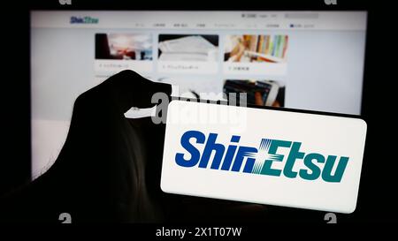 Person mit Handy mit Logo des japanischen Chemieunternehmens Shin-Etsu Chemical Co. Ltd. Vor der Webseite. Schwerpunkt auf dem Display des Telefons. Stockfoto