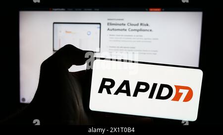 Person, die ein Mobiltelefon mit dem Logo des amerikanischen Cybersicherheitsunternehmens Rapid7 vor der Business-Webseite hält. Schwerpunkt auf dem Display des Telefons. Stockfoto