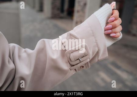 Modische Details eines beigefarbenen Trenchcoat-Ärmchens für Damen, weibliche Hand mit rosa Maniküre Stockfoto
