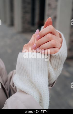 Modische Details eines gestrickten weißen Pullover-Ärmeln, weibliche Hände mit rosa Maniküre Stockfoto