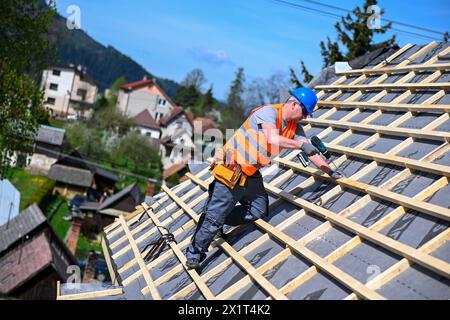 Reparatur und Austausch des alten Dachs durch ein neues. Bauarbeiter in Schutzkleidung, der mit Werkzeugen auf dem Dach steht. Stockfoto