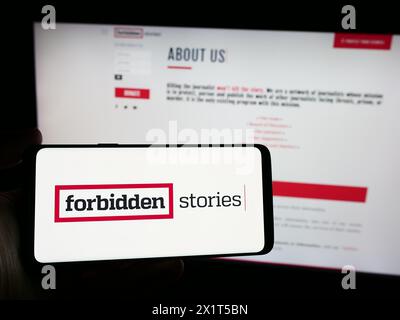 Person, die ein Smartphone mit dem Logo der investigativen Journalismusorganisation Forbidden Stories vor der Website hält. Schwerpunkt auf dem Display des Telefons. Stockfoto