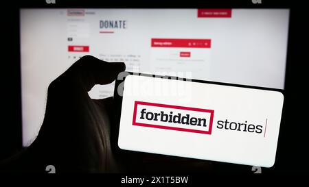Person, die ein Mobiltelefon mit dem Logo der investigativen Journalismusorganisation Forbidden Stories vor der Webseite hält. Schwerpunkt auf dem Display des Telefons. Stockfoto