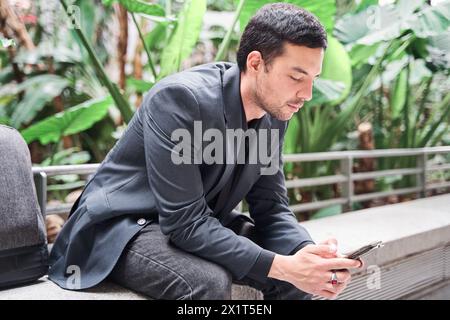 Junger latino-Geschäftsmann, der auf sein Smartphone schaut, während er wartet Stockfoto