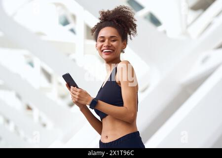 Die Frau lächelt glücklich, während sie draußen auf ihr Handy blickt Stockfoto