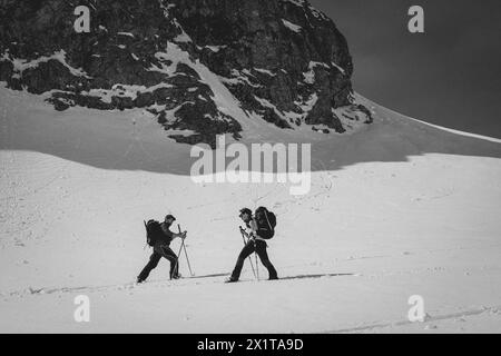 Athleten, die an einem sonnigen Tag im Hinterland Ski fahren, mit einer Landschaft aus verschneiten Bergen. Schwarz-weiß. Stockfoto