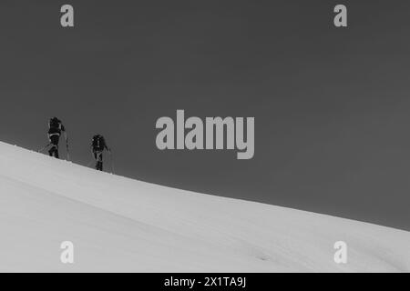 Athleten, die an einem sonnigen Tag im Hinterland Ski fahren, mit einer Landschaft aus verschneiten Bergen. Schwarz-weiß. Stockfoto