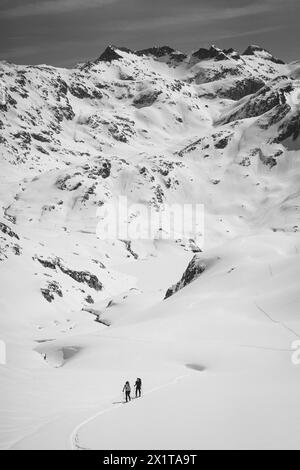 Athleten, die an einem sonnigen Tag im Hinterland Ski fahren, mit einer Landschaft aus verschneiten Bergen. Schwarz-weiß. Stockfoto