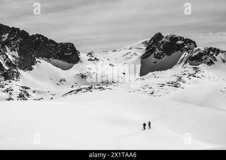 Athleten, die an einem sonnigen Tag im Hinterland Ski fahren, mit einer Landschaft aus verschneiten Bergen. Schwarz-weiß. Stockfoto