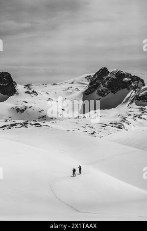 Athleten, die an einem sonnigen Tag im Hinterland Ski fahren, mit einer Landschaft aus verschneiten Bergen. Schwarz-weiß. Stockfoto