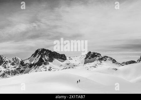 Athleten, die an einem sonnigen Tag im Hinterland Ski fahren, mit einer Landschaft aus verschneiten Bergen. Schwarz-weiß. Stockfoto