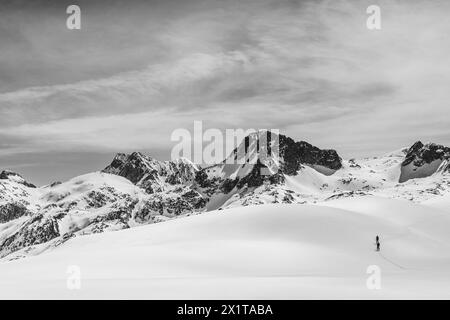 Athleten, die an einem sonnigen Tag im Hinterland Ski fahren, mit einer Landschaft aus verschneiten Bergen. Schwarz-weiß. Stockfoto