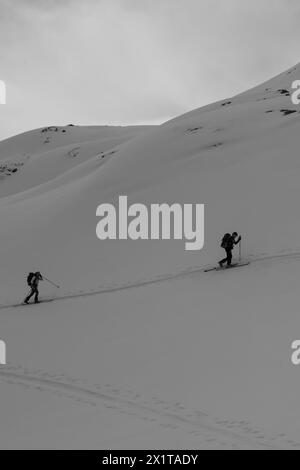 Athleten, die an einem sonnigen Tag im Hinterland Ski fahren, mit einer Landschaft aus verschneiten Bergen. Schwarz-weiß. Stockfoto