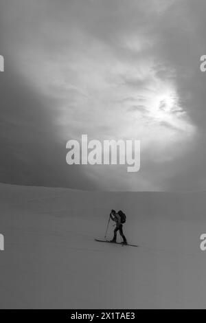 Athleten, die an einem sonnigen Tag im Hinterland Ski fahren, mit einer Landschaft aus verschneiten Bergen. Schwarz-weiß. Stockfoto