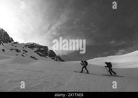 Athleten, die an einem sonnigen Tag im Hinterland Ski fahren, mit einer Landschaft aus verschneiten Bergen. Schwarz-weiß. Stockfoto