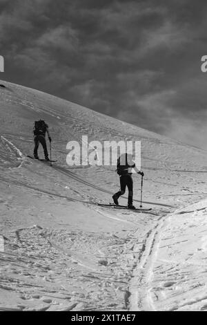 Athleten, die an einem sonnigen Tag im Hinterland Ski fahren, mit einer Landschaft aus verschneiten Bergen. Schwarz-weiß. Stockfoto