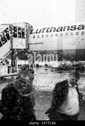 Frankfurt, Deutschland - 4. Mai 2019: Fluggäste werden in Glas reflektiert und steigen in ein Lufthansa-Flugzeug auf regnerischer Asphaltbahn ein Stockfoto