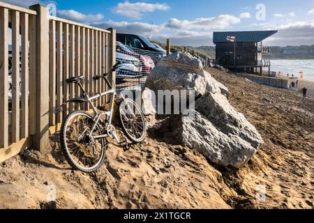 Ein Fahrrad, das an einem Holzzaun am Fistral Beach in Newquay in Cornwall in Großbritannien befestigt ist. Stockfoto