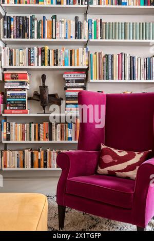 Pinkfarbener Sessel mit Bücherregalen in Chelsea HOME, London, Großbritannien Stockfoto