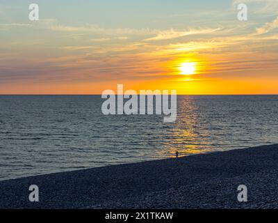 Eine Silhouette einer Einzelfigur, die am Meeresrand steht, wenn die Sonne untergeht. Enthält Platz für Text Stockfoto