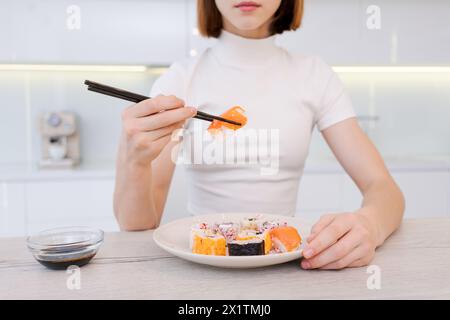 Die Frau isst Sushi mit Essstäbchen. Der Teller ist voller Sushi und auf dem Tisch steht eine kleine Schüssel Sojasauce. Die Frau konzentriert sich auf ihre Mahlzeit und Th Stockfoto