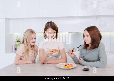 Die Frau füttert ihren beiden Töchtern Sushi. Die Szene ist glücklich und familienorientiert Stockfoto