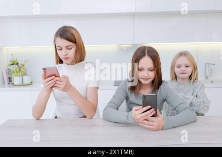 Drei Mädchen sitzen am Tisch und schauen sich ihre Handys an. Die Szene ist lässig und entspannt, da die Mädchen keine anderen Aktivitäten ausüben Stockfoto