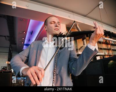 Musiker in Geschäftskleidung, spielt elektronische Geige mit intensivem Fokus. Stockfoto