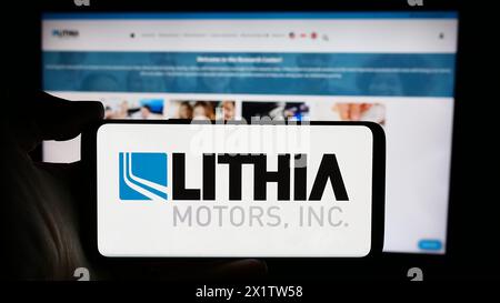 Person, die ein Mobiltelefon mit dem Logo des US-amerikanischen Autohändlers Lithia Motors Inc. Vor der Website des Unternehmens hält. Schwerpunkt auf dem Display des Telefons. Stockfoto