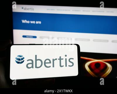 Person mit Smartphone und Logo des spanischen Mautunternehmens Abertis Infraestructuras S.A. vor der Website. Schwerpunkt auf dem Display des Telefons. Stockfoto