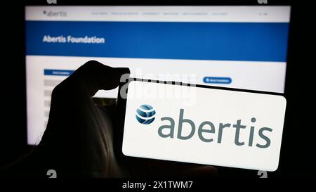 Person, die ein Mobiltelefon mit dem Logo des spanischen Mautunternehmens Abertis Infraestructuras SA vor der Website hält. Schwerpunkt auf dem Display des Telefons. Stockfoto