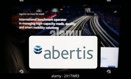 Person, die ein Mobiltelefon mit dem Logo des spanischen Mautunternehmens Abertis Infraestructuras S.A. vor der Webseite hält. Schwerpunkt auf dem Display des Telefons. Stockfoto