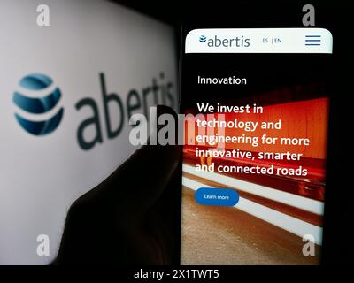 Person, die ein Mobiltelefon mit Webseite des spanischen Mautunternehmens Abertis Infraestructuras S.A. mit Logo hält. Konzentrieren Sie sich auf die Mitte des Telefondisplays. Stockfoto