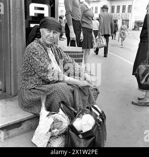 Die Sozialistische Republik Rumänien in den 1970er Jahren Eine ältere Frau mit zwei Taschen Lebensmittel, die vor einem Lebensmittelgeschäft in der Stadt warten. Stockfoto