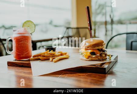 Köstlicher Hamburger mit Pommes frites und Erdbeercocktail auf einem Holztisch. Hamburger mit Erdbeercocktail auf dem Tisch Stockfoto