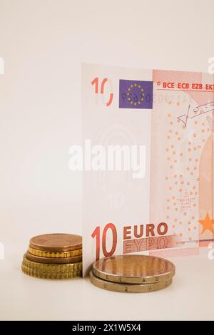 Nahaufnahme von 10 Euro Banknote und Stapel von verschiedenen Gold- und kupferfarbenen Münzen auf weißem Hintergrund, Studiokomposition, Quebec, Kanada Stockfoto