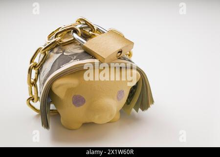 Nahaufnahme von Banknoten der US-Währung, die mit einer Messingkette und einem Schloss um eine gelbe Schweinebank auf weißem Hintergrund gewickelt sind, Studio Stockfoto